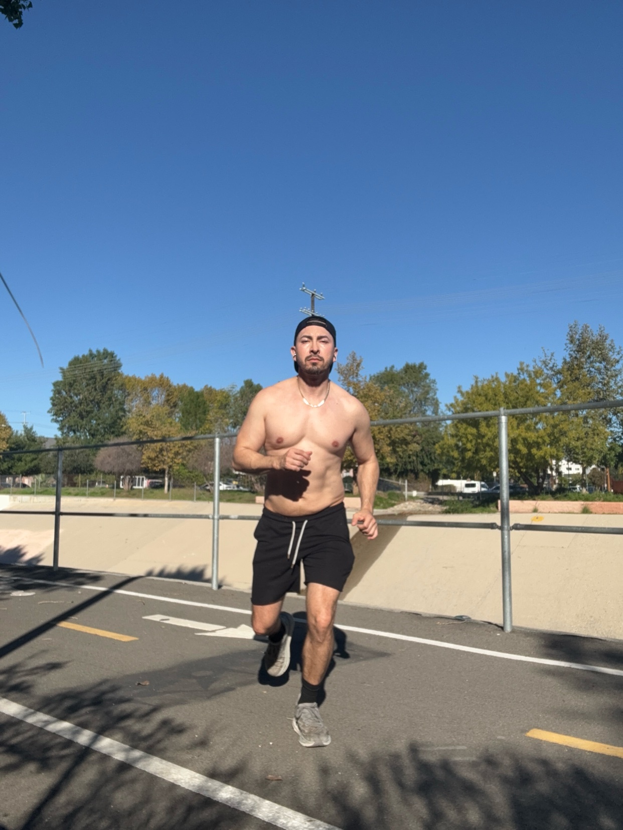 A man runs shirtless on a paved path. The photo is taken from a low angle, with a clear blue sky in the background.