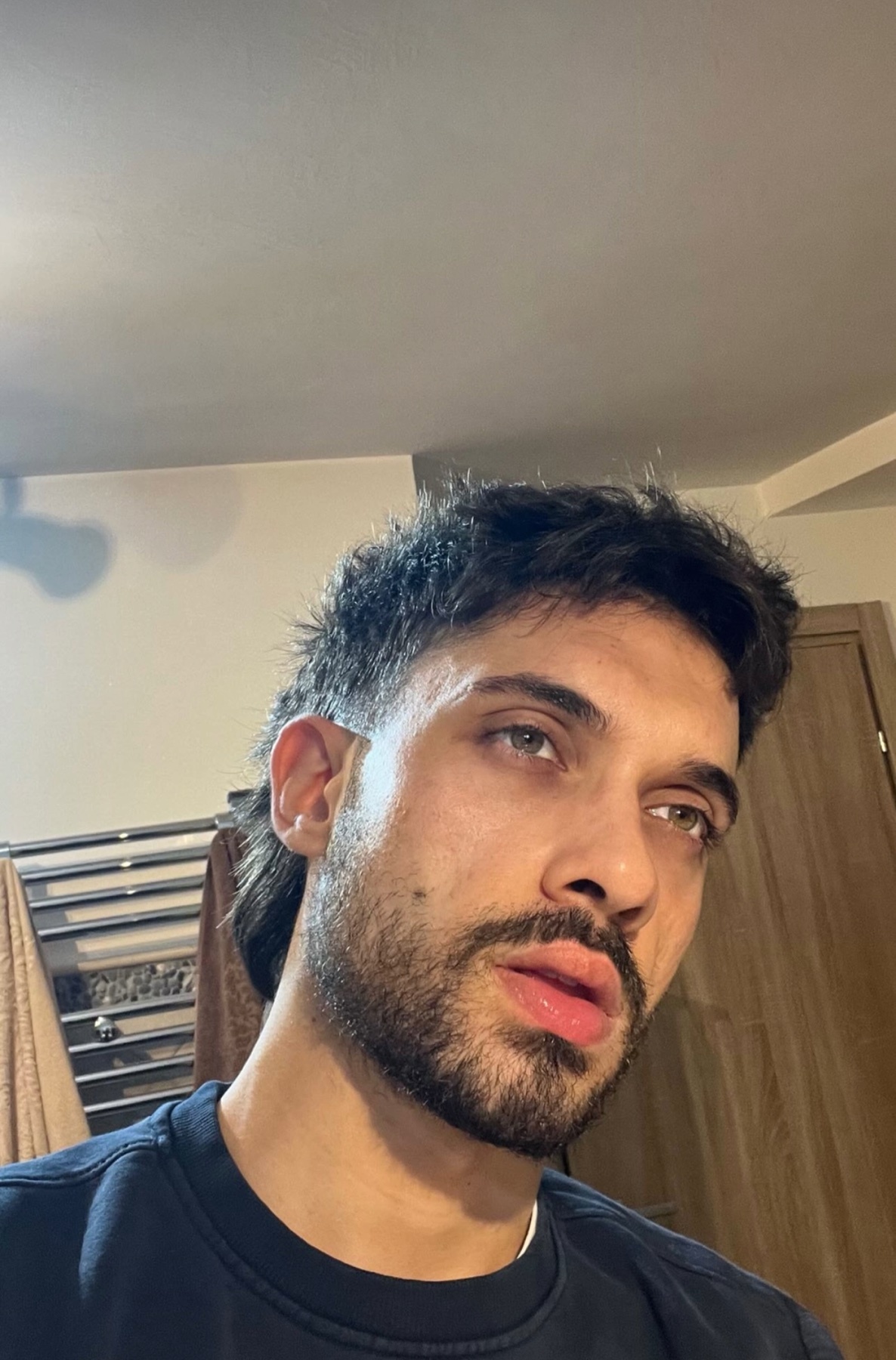 A close-up selfie of a man with a mullet and a beard. He is looking off to the side with his mouth slightly open.