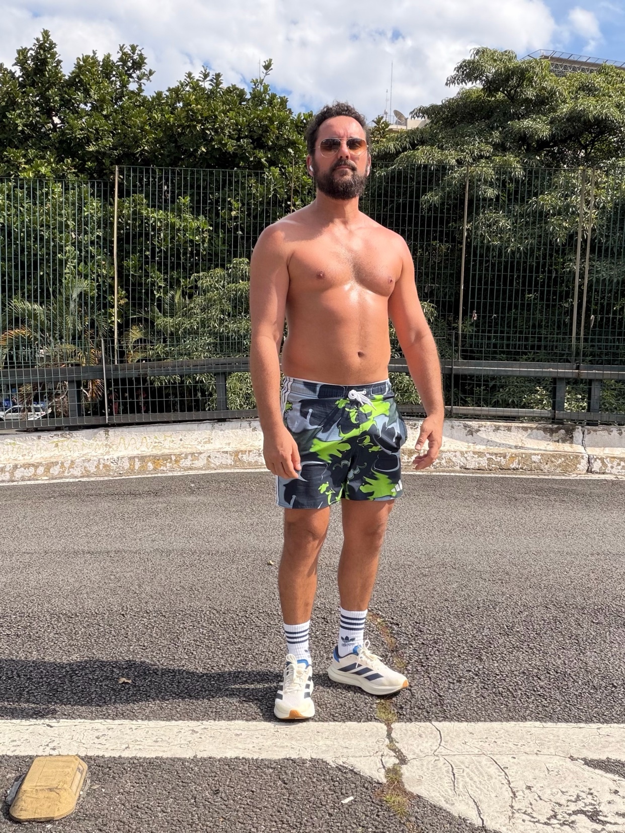 A shirtless man with a beard stands outdoors wearing camouflage shorts and athletic shoes, ready for a run.