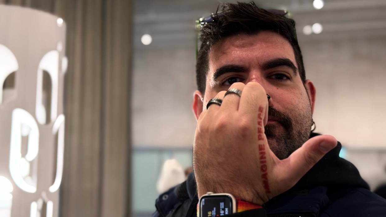 A man with a tattoo that says "Imagine Peace" on his hand. He is wearing a watch and rings.