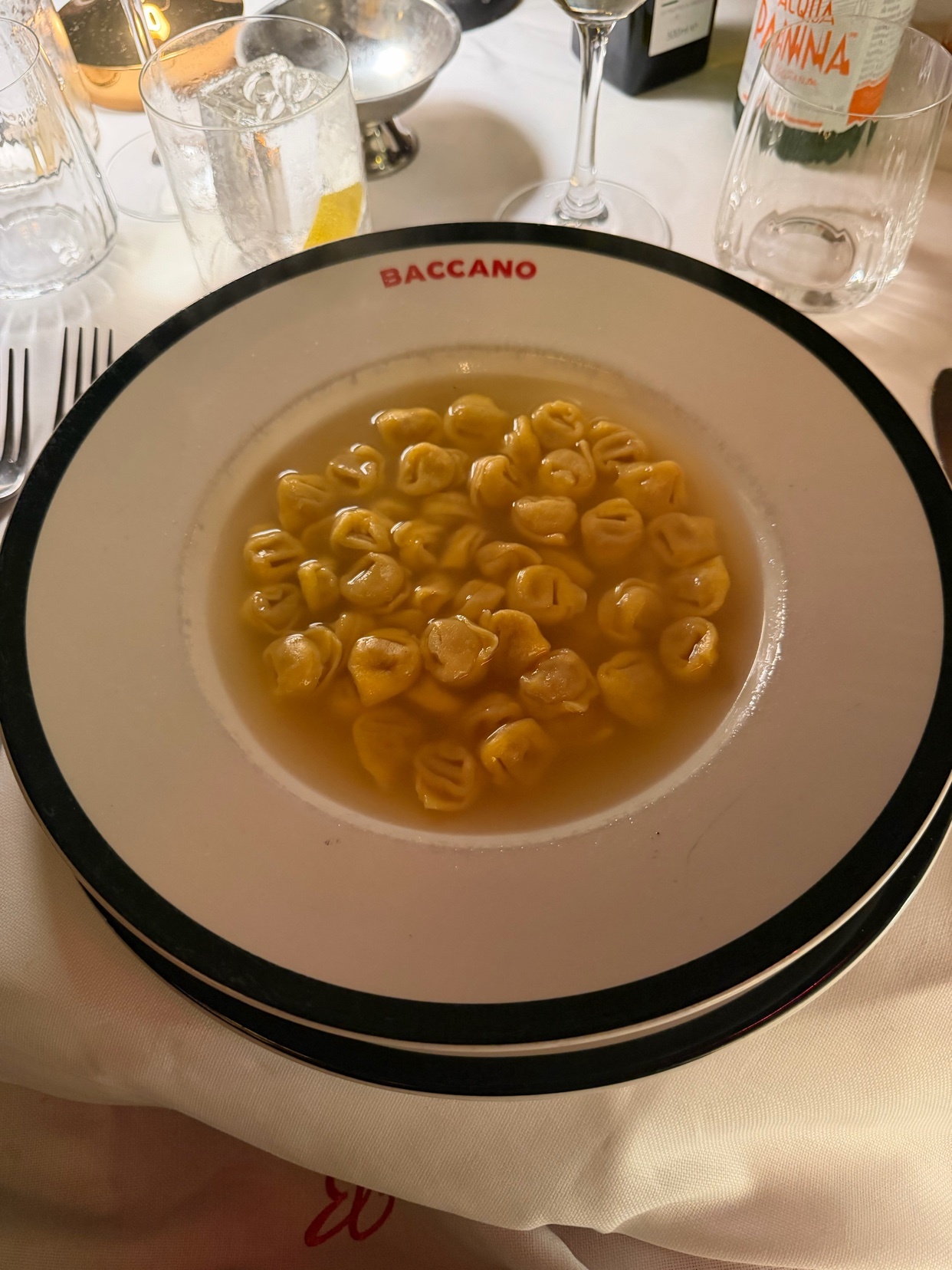 A close-up shot of a plate of tortellini soup at a restaurant. The soup is served in a white bowl with a black rim.