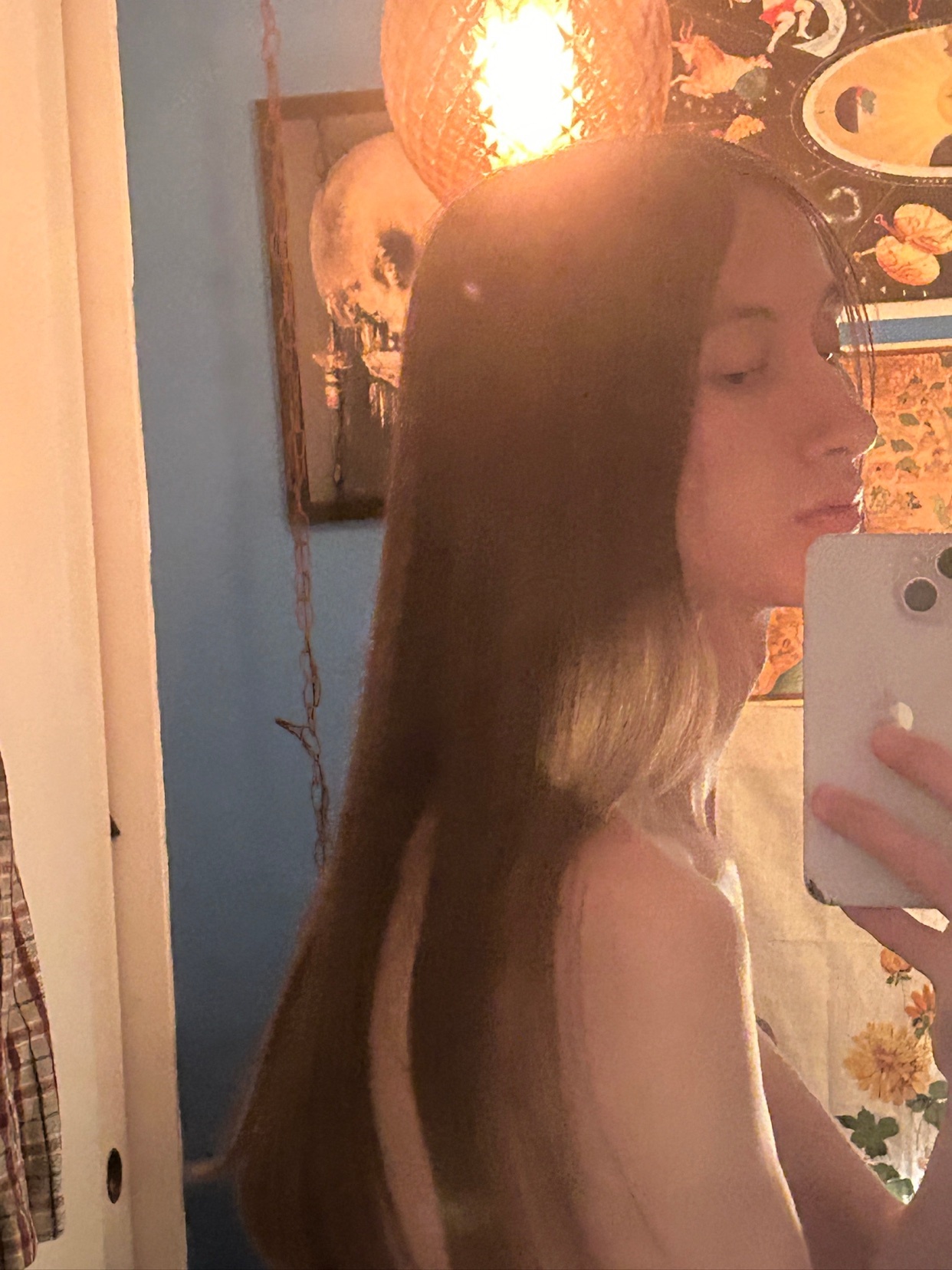 A woman takes a mirror selfie, showcasing her long, flowing hair. The photo is taken from the side, with the woman's shoulder and upper body visible.