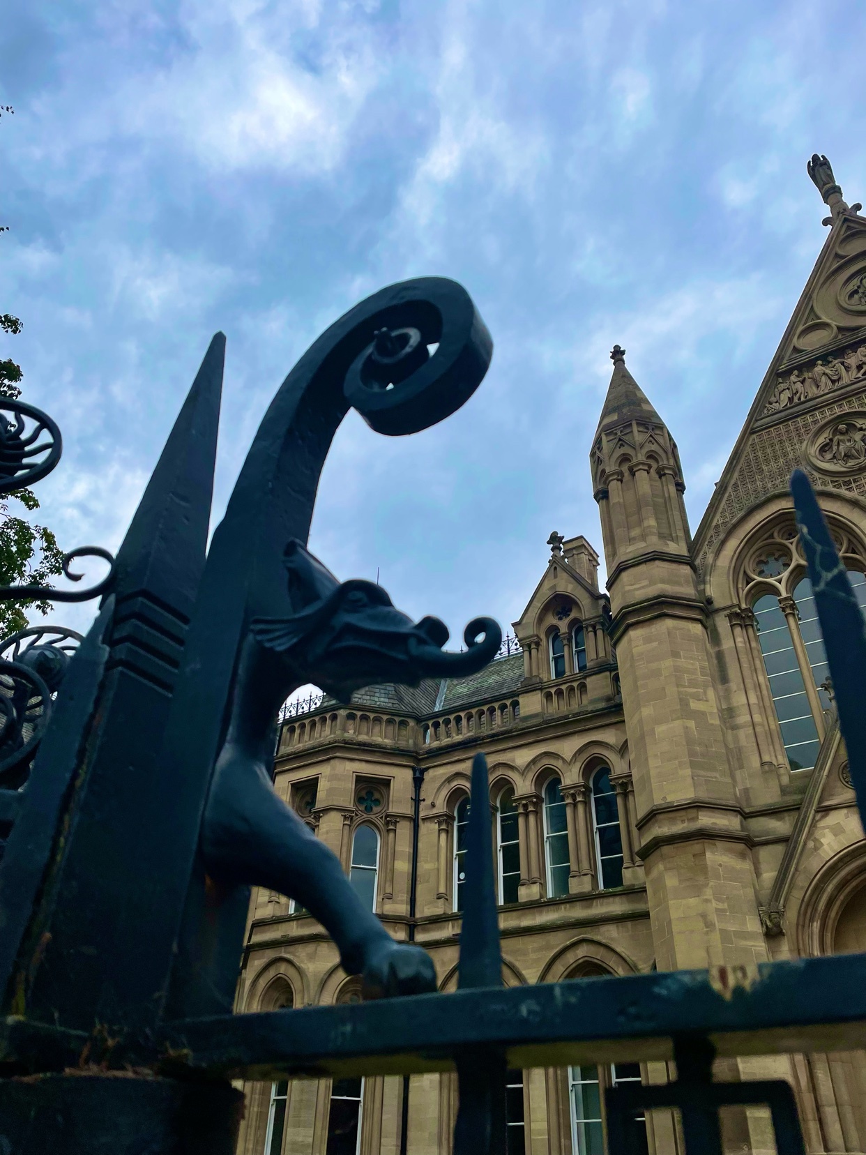 A low-angle shot captures a detailed view of a decorative metal gate featuring a dragon sculpture, with a historic building in the background. The image highlights the intricate design of the gate and the architectural details of the building.