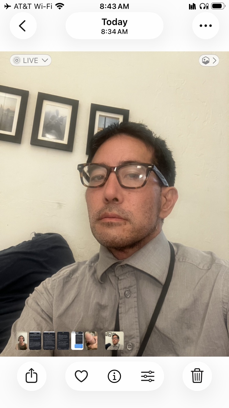 A man with glasses and a button-down shirt takes a selfie.