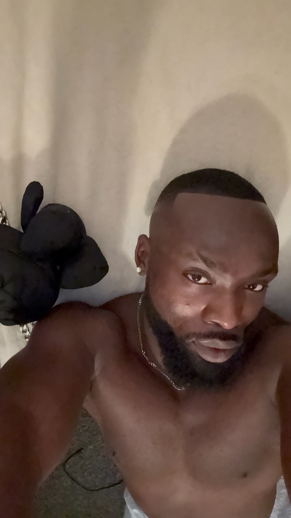 A shirtless Black man takes a selfie. He has a beard and dark hair.