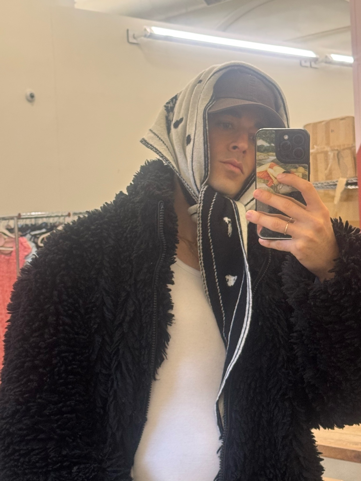 A man takes a mirror selfie, wearing a black jacket and a bandana. The photo showcases a modern and stylish look.