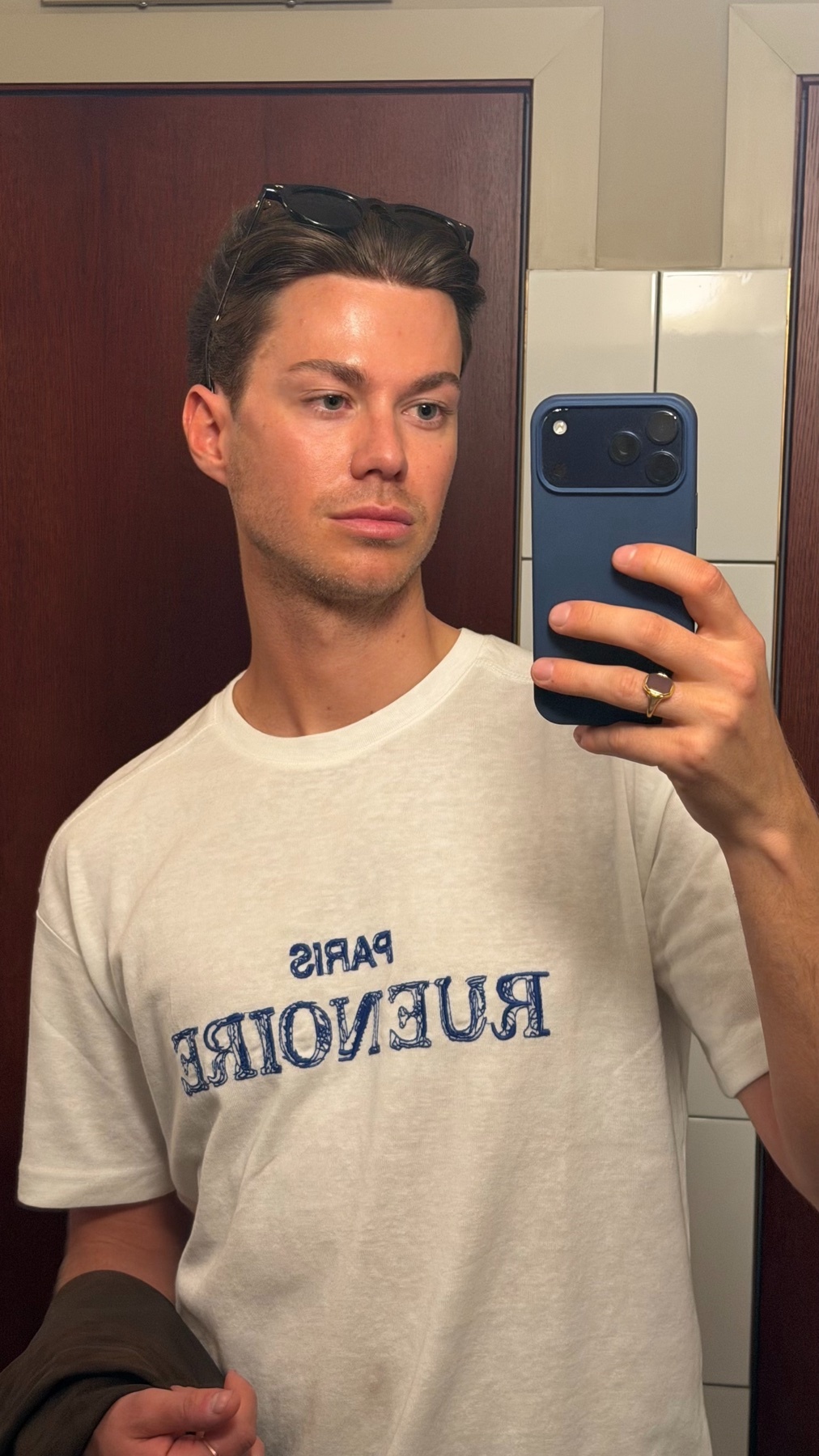 A man takes a selfie in a white t-shirt with sunglasses on his head.