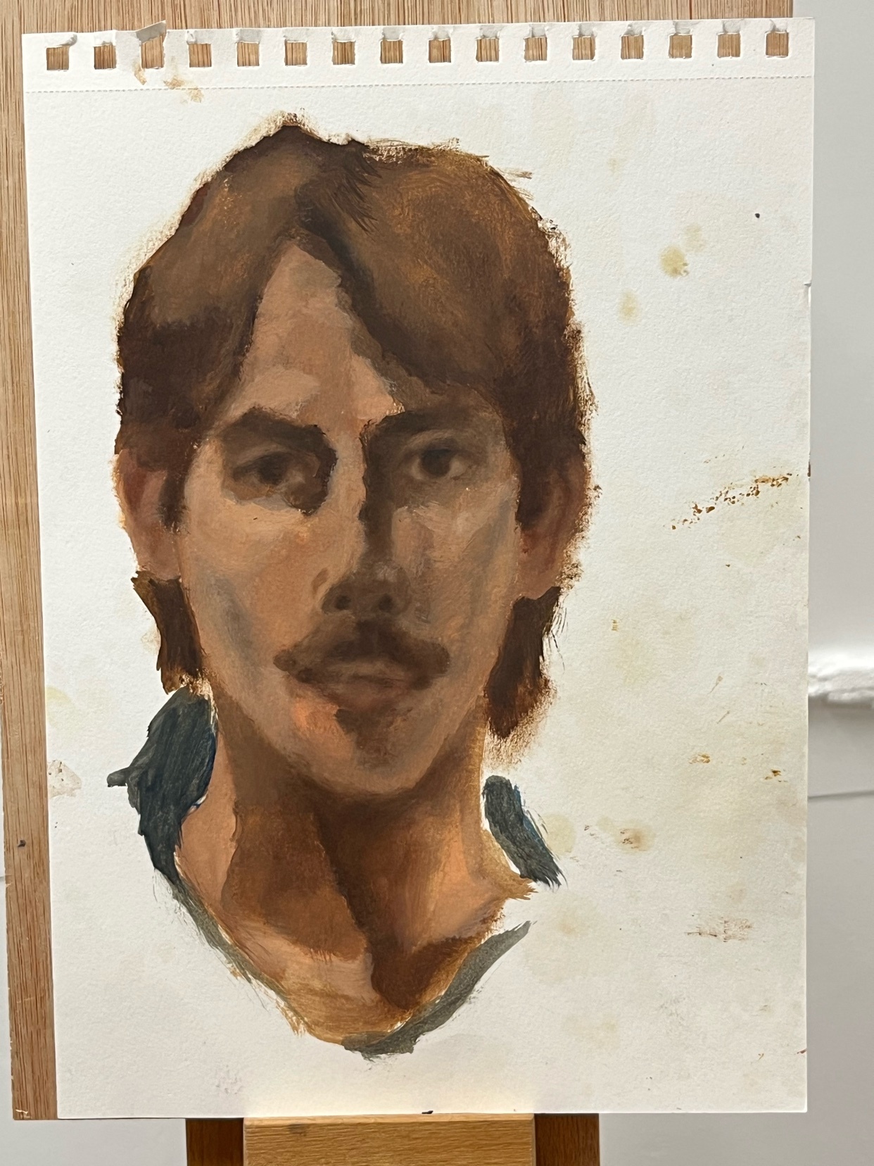 A painting of a man with a mustache and brown hair is displayed on an easel. The artwork is a portrait with visible brushstrokes and a light background.
