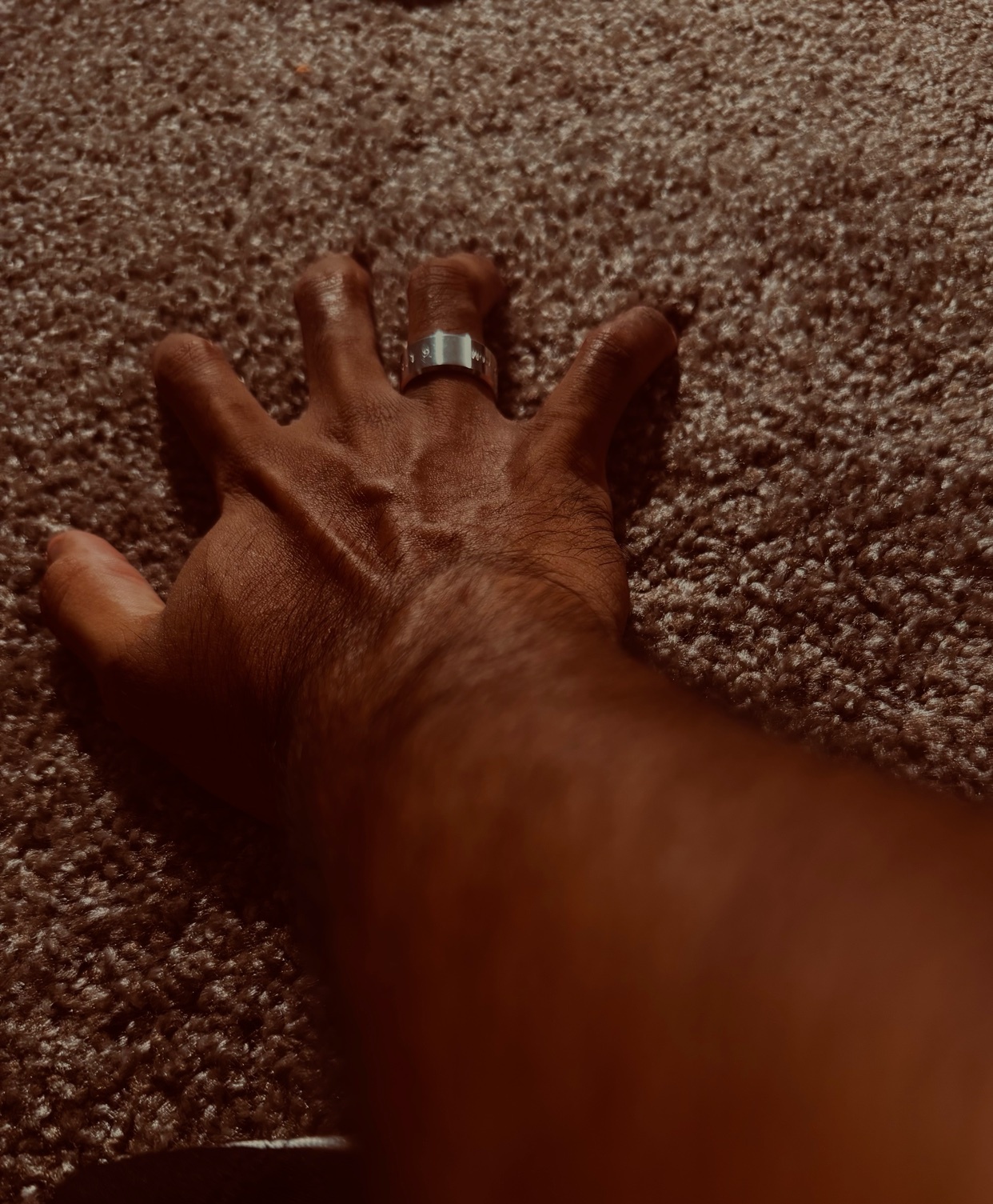 A close-up shot of a man's hand with a ring on one finger. The hand is outstretched, with veins visible.