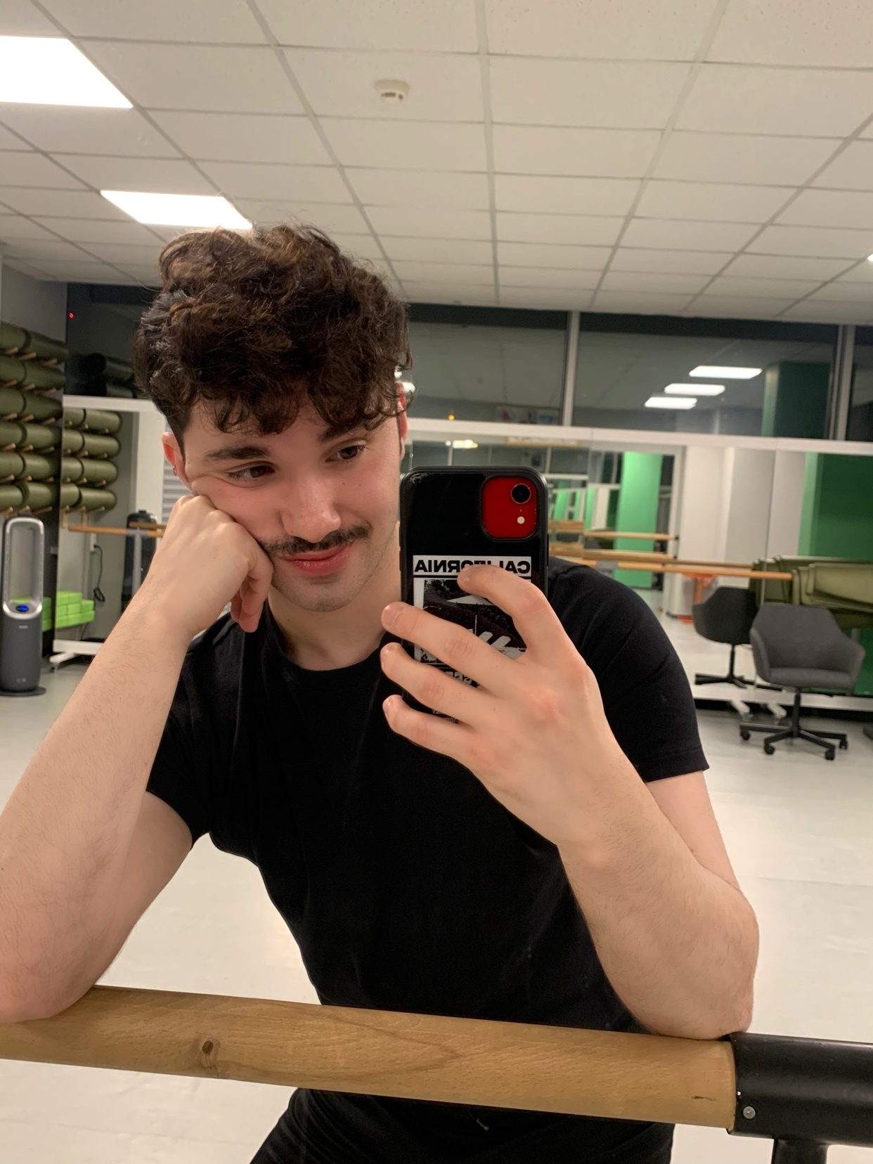 A man takes a selfie in a dance studio. He is leaning on a ballet barre.