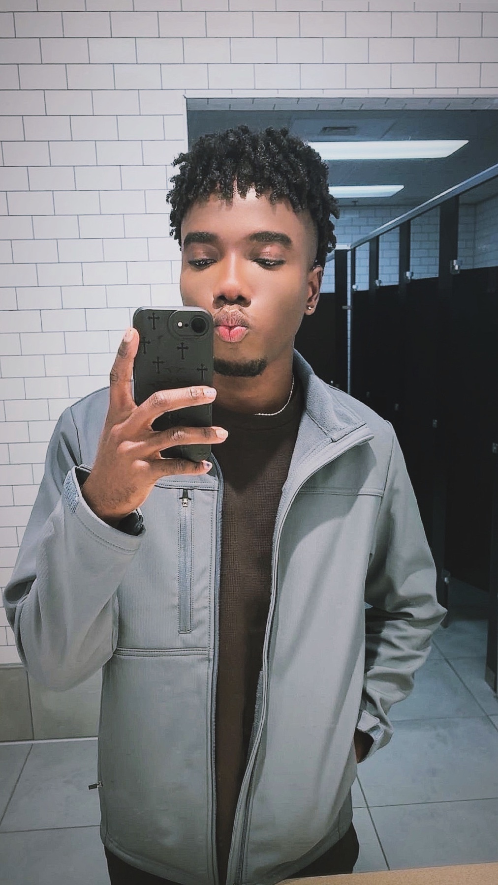 A young black man takes a selfie in a public restroom, puckering his lips and looking at the camera.