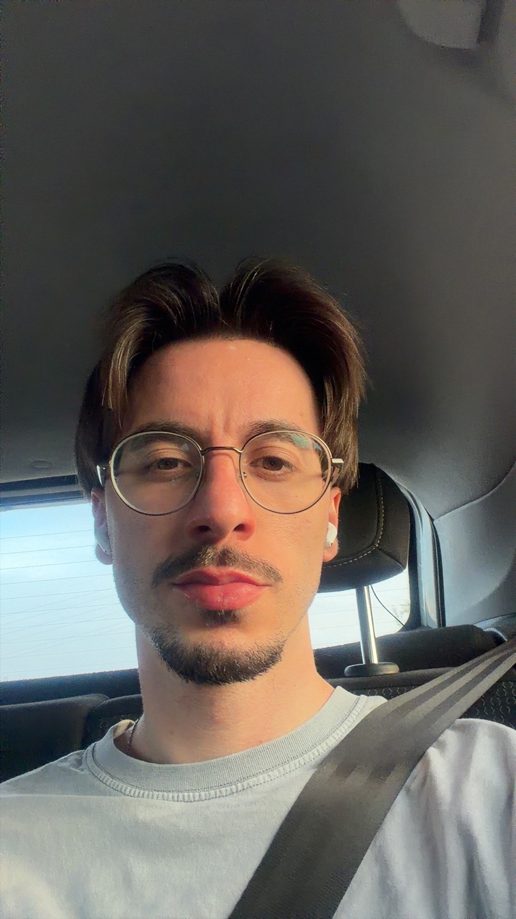 A man with glasses and a mustache takes a selfie in a car.