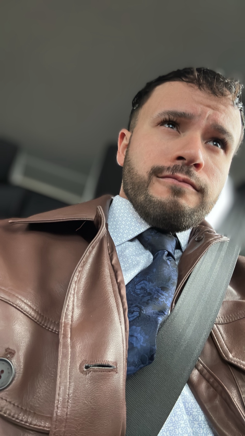 A man in a brown leather jacket and tie looks up. The photo is taken from a low angle.