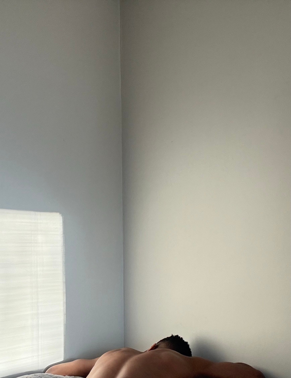 A man is lying shirtless against a wall. The photo has a minimalist aesthetic.