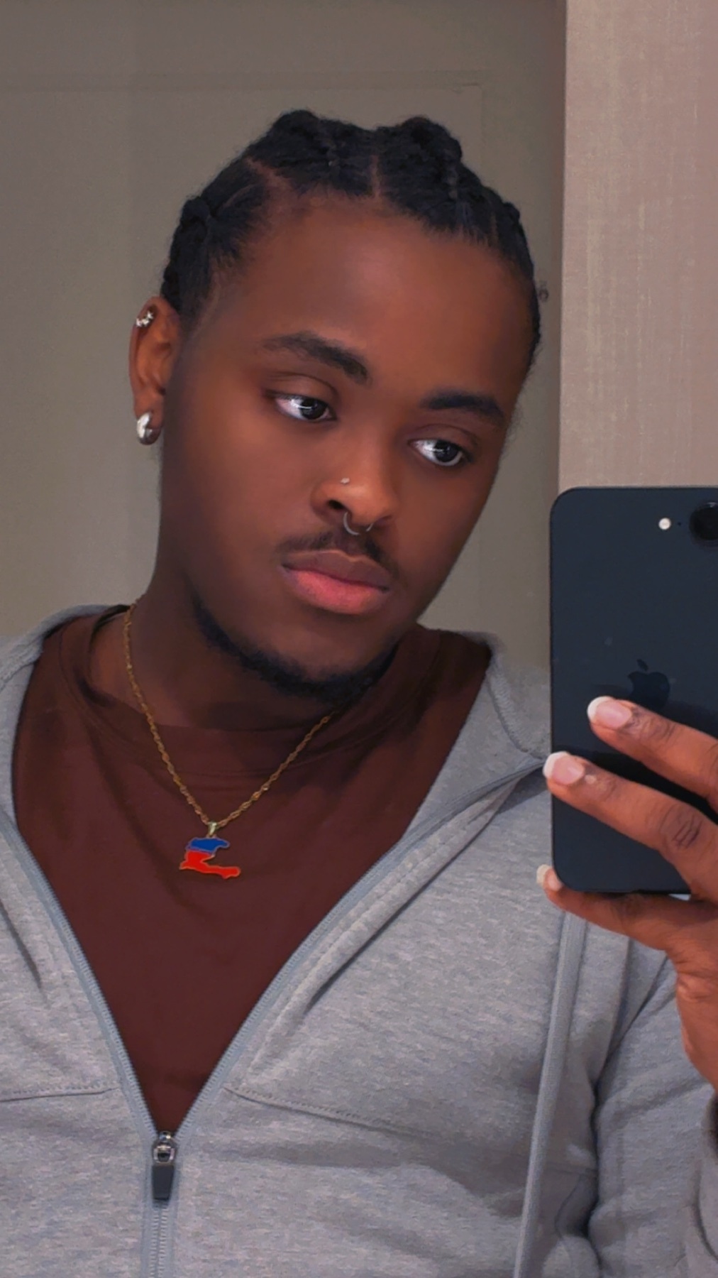 A man takes a selfie in a mirror. He is wearing a brown shirt and a grey hoodie.