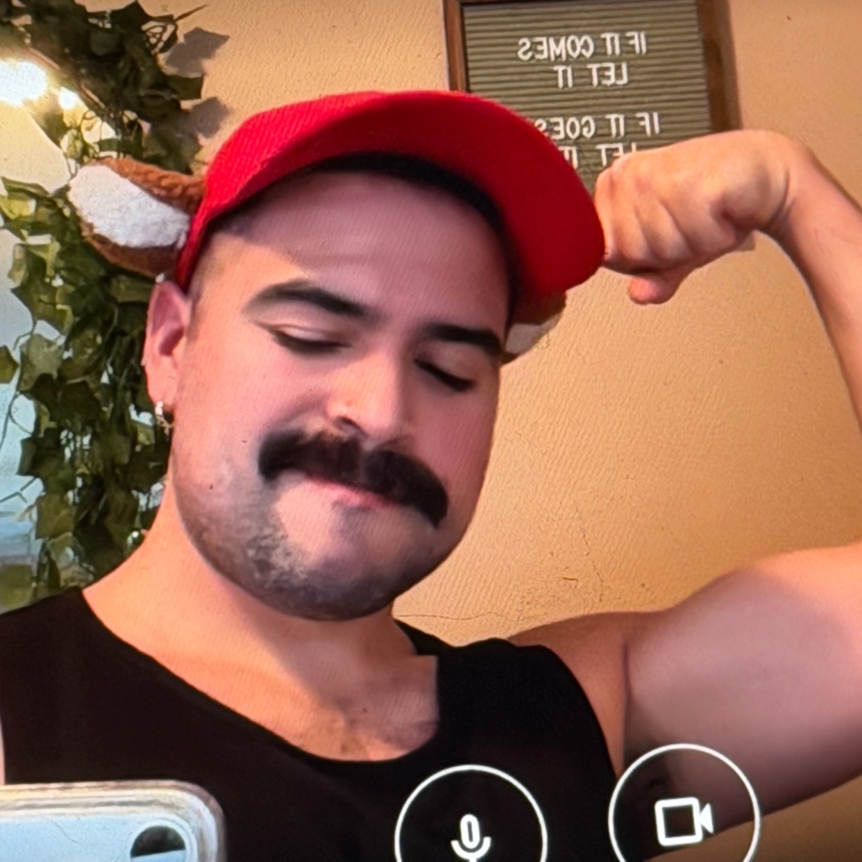 A man flexes his bicep while wearing a cap. The image is a selfie.
