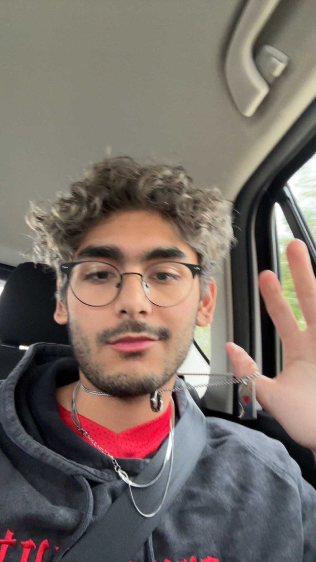 A selfie of a man with curly hair, glasses, and a neck tattoo. He is wearing a hoodie and a necklace.