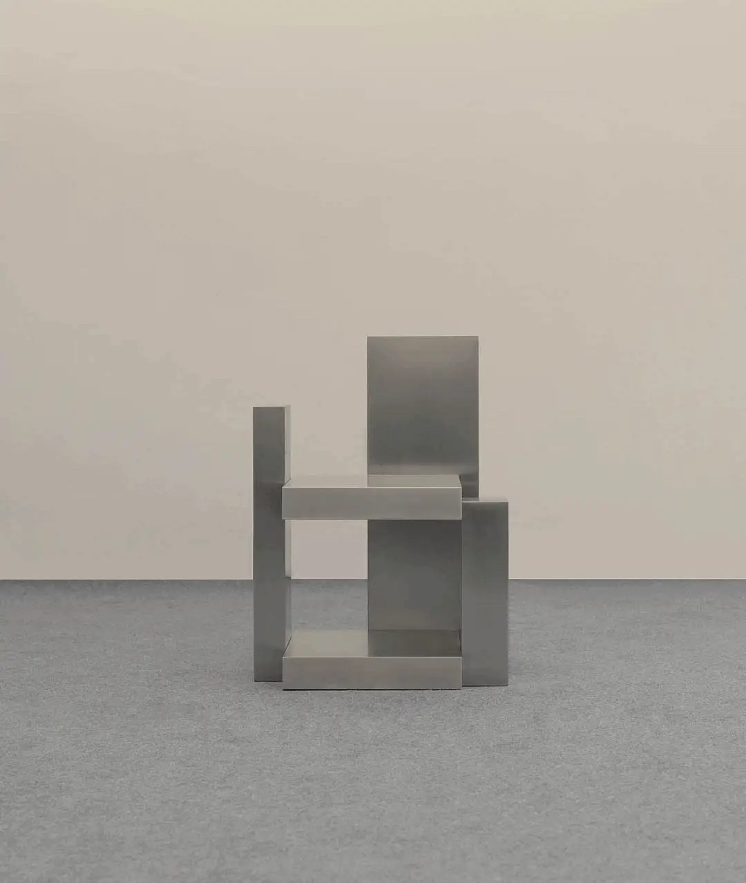 A modern, minimalist chair with a geometric design. The chair is made of a gray material and is set against a neutral background.