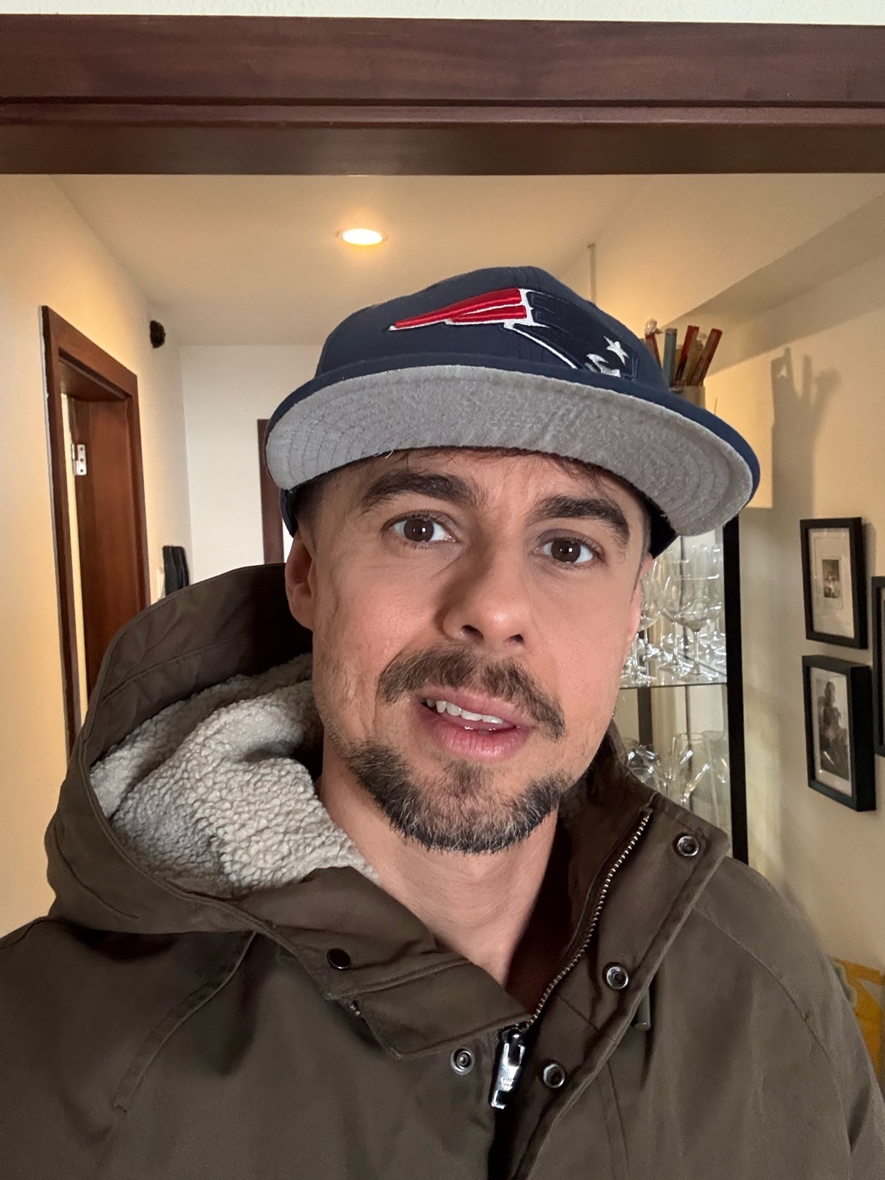 A man wearing a cap and jacket poses for a photo indoors. The man is looking directly at the camera.
