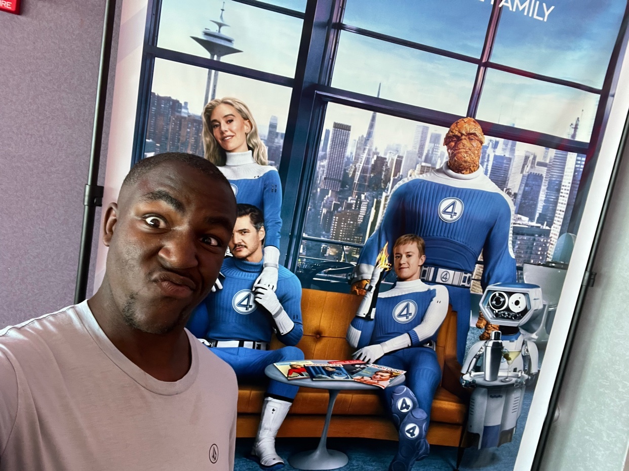 A man takes a selfie in front of a Fantastic Four movie poster. The man is making a funny face.