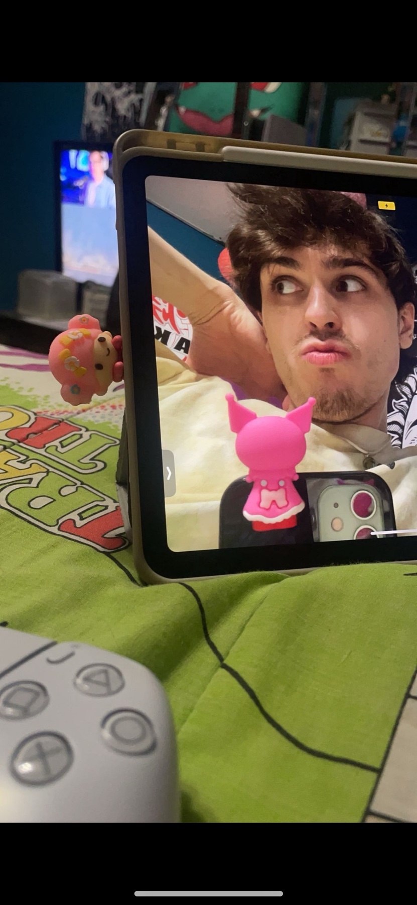 A young man makes a funny face while taking a selfie with his tablet. A video game controller is visible in the foreground.