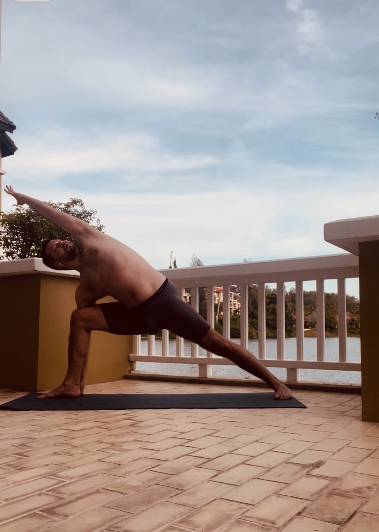 A man is doing yoga on a patio. He is shirtless and in a yoga pose.