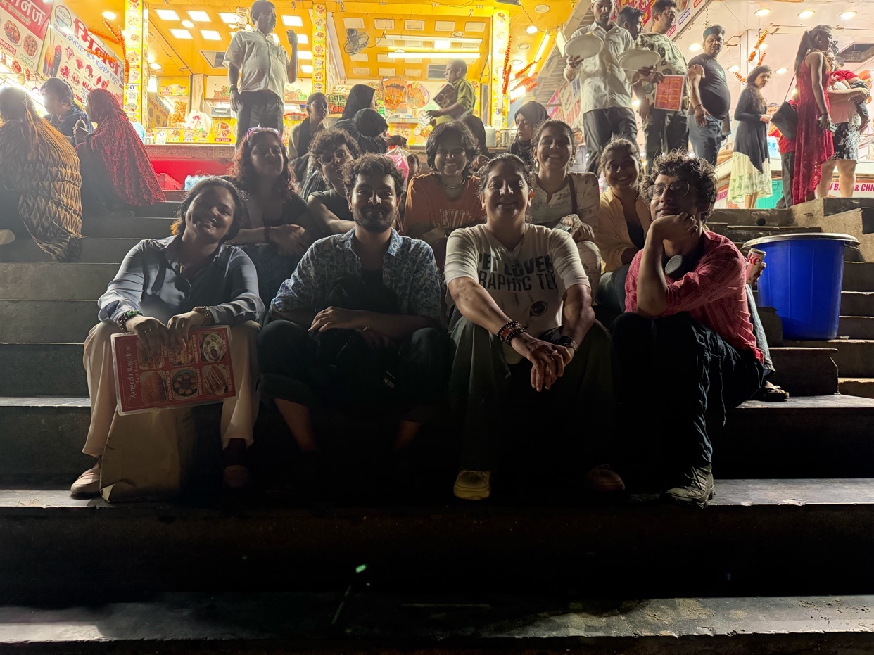 A group of people are sitting on steps at night. They are smiling and appear to be enjoying each other's company.