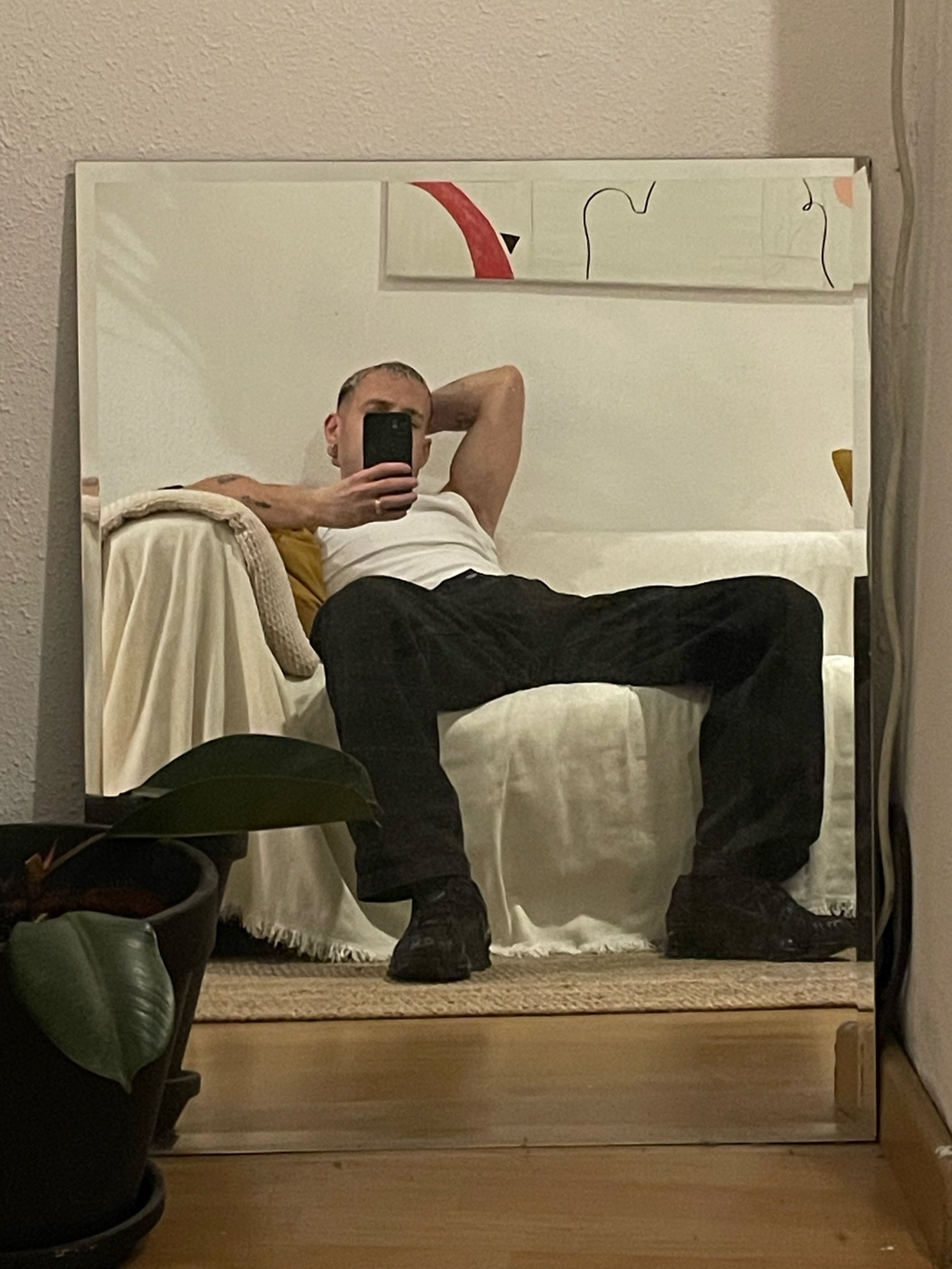 A man takes a mirror selfie, showcasing his style. He's shirtless, wearing black pants, and posing indoors.