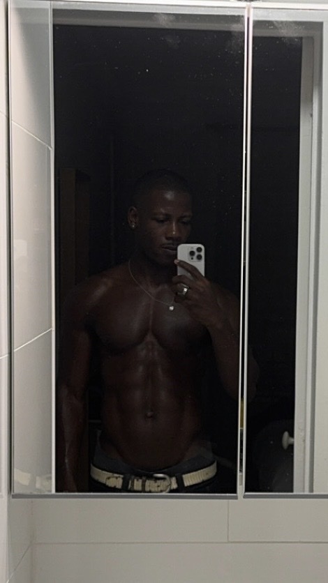 A man takes a mirror selfie, showcasing his muscular physique. He is shirtless, highlighting his abs and chest hair.