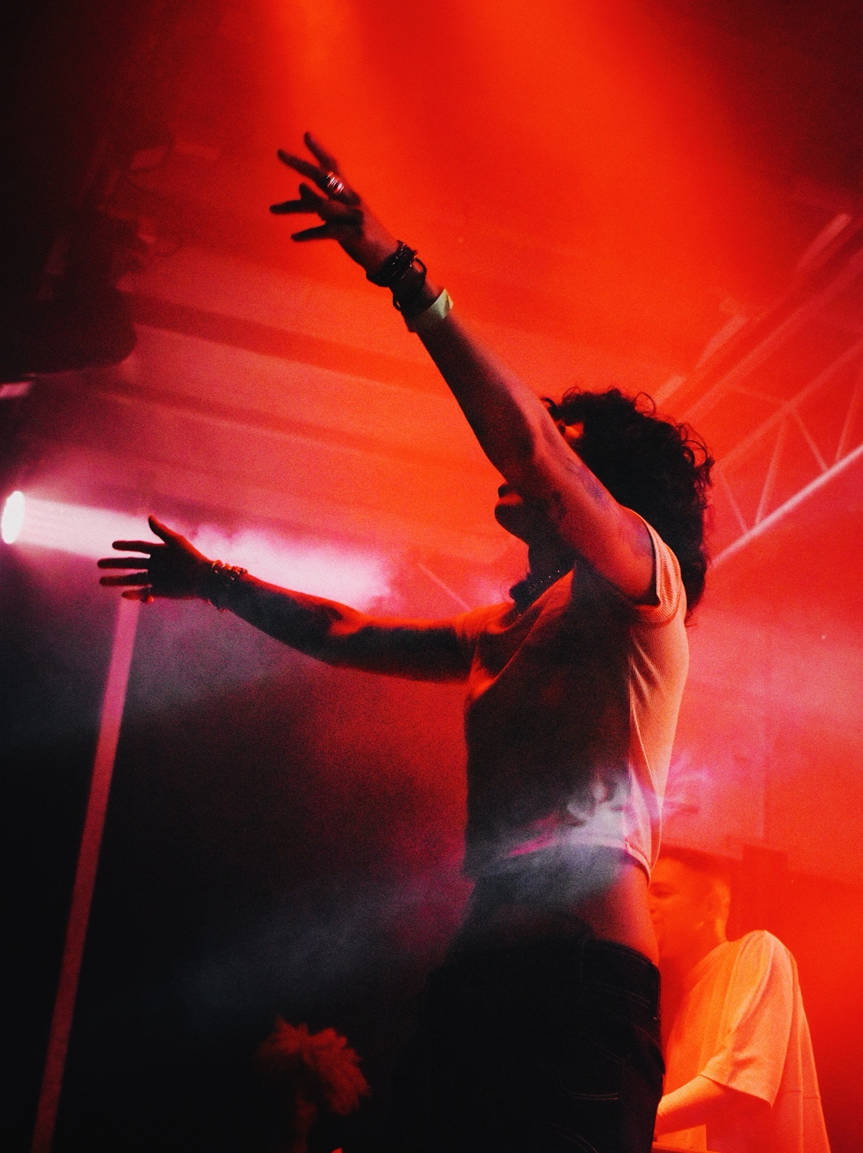 A silhouette of a man with his arms raised in a concert setting. The stage is lit with red lights.