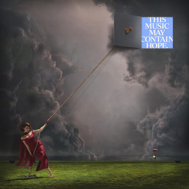 A woman in a flowing red dress pulls a rope attached to an open box floating in a dramatic, cloudy sky. The box contains the text "THIS MUSIC MAY CONTAIN HOPE."