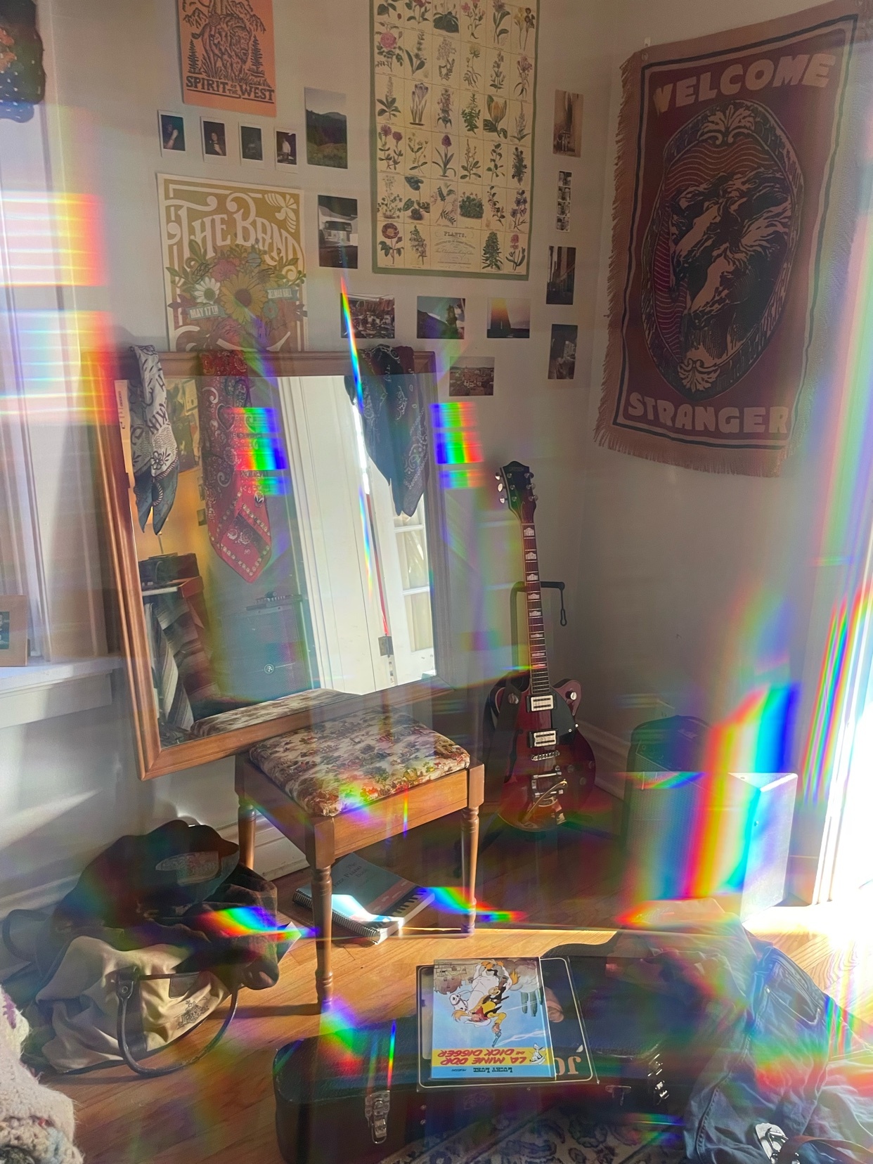 A room is filled with bohemian decor, including a tapestry, a guitar, and various wall art. Rainbow light streams in from the side, illuminating the space.