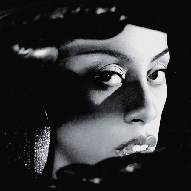 A striking black and white portrait of a woman. She is looking directly at the camera with a captivating gaze.