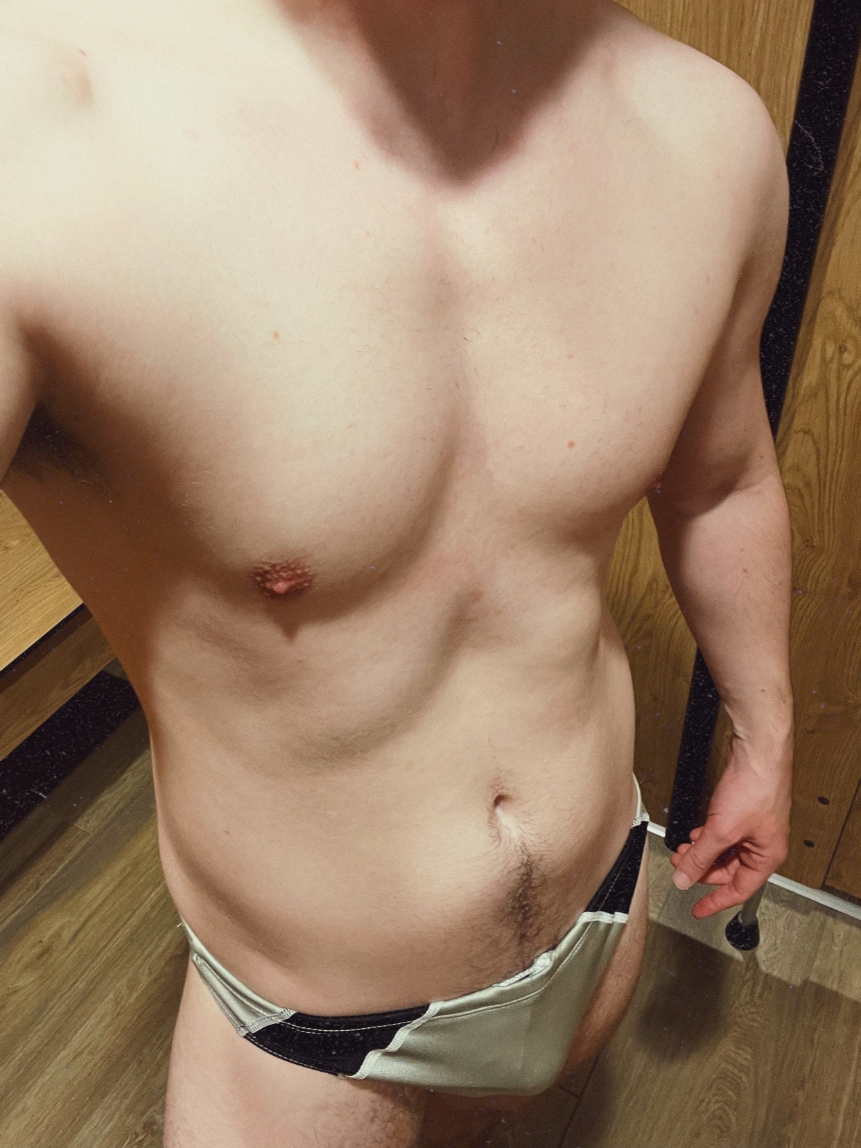 A man poses shirtless, wearing swimwear. The photo focuses on his physique.