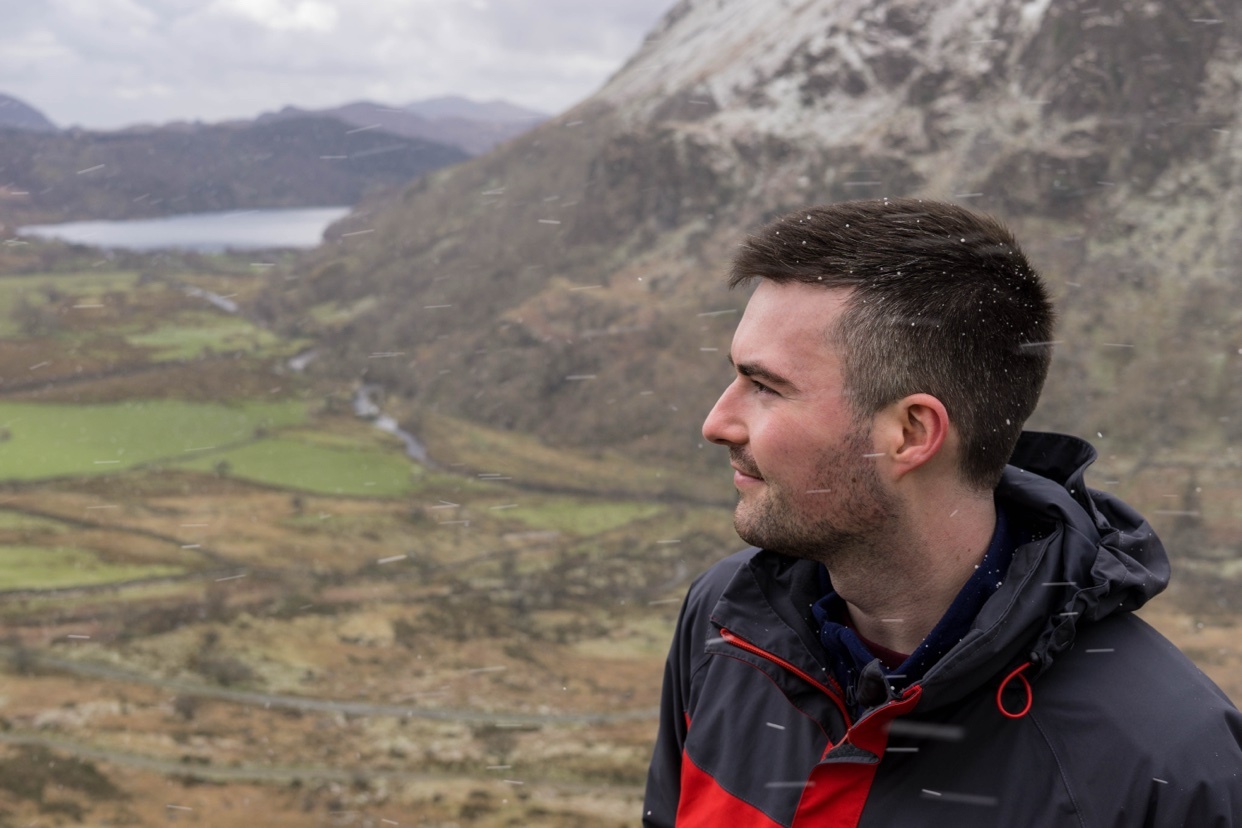 A man looks out over a snowy mountain landscape. The photo captures a scenic view of Snowdonia in North Wales.
