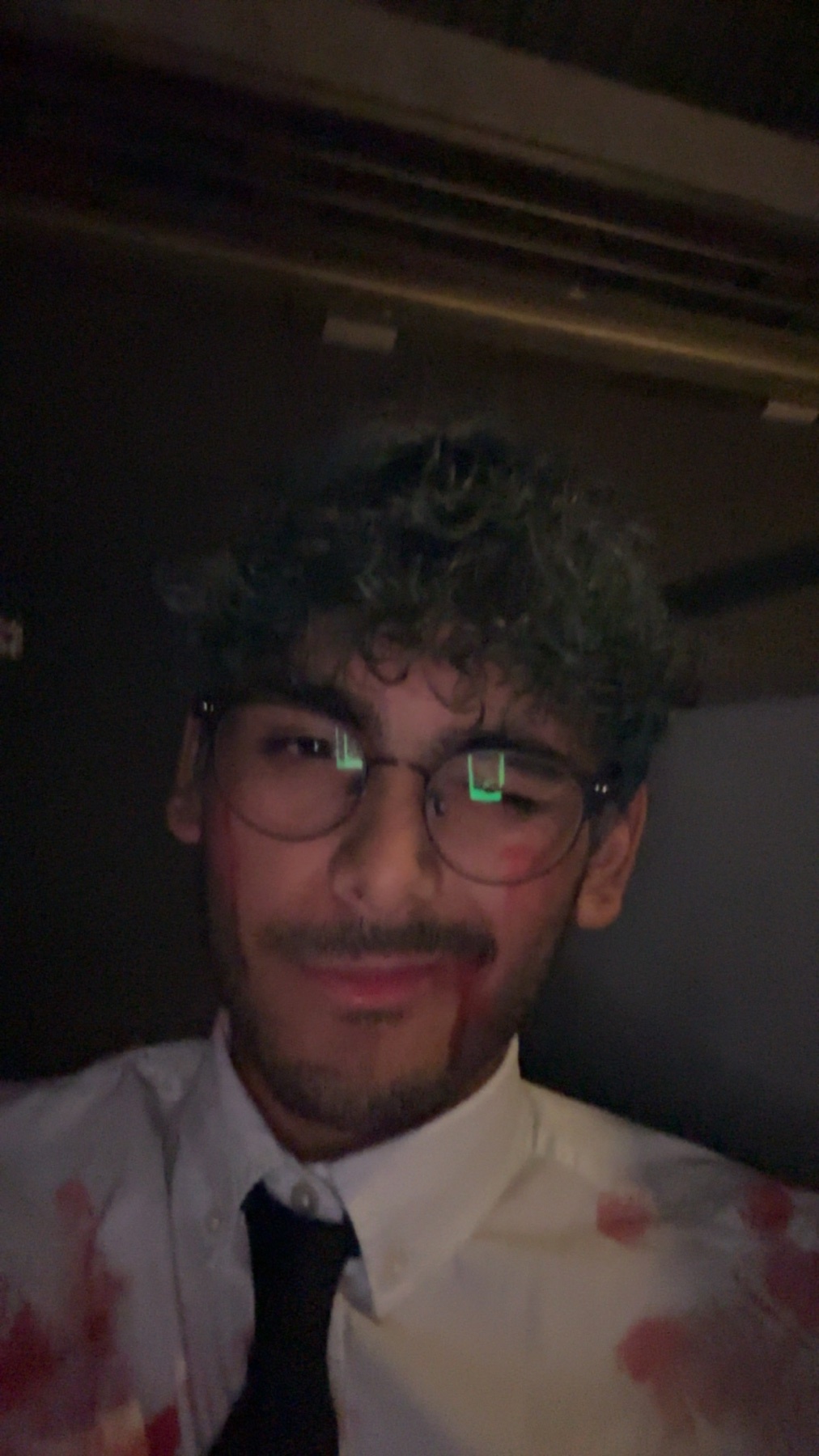 A man in a costume with fake blood on his face. He is wearing glasses and a white shirt with a black tie.