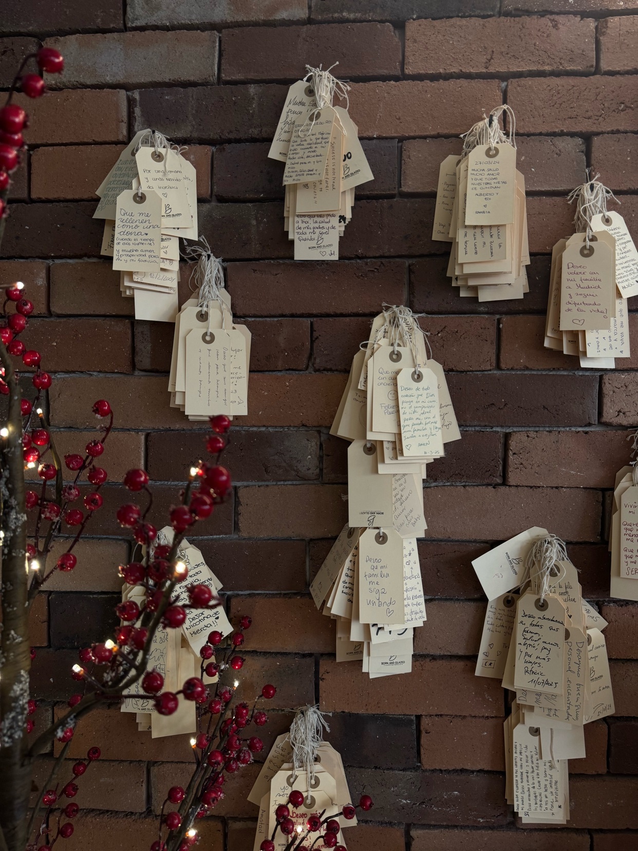 A brick wall is decorated with vintage tags, some with writing on them. Red berries and Christmas decor add to the holiday theme.