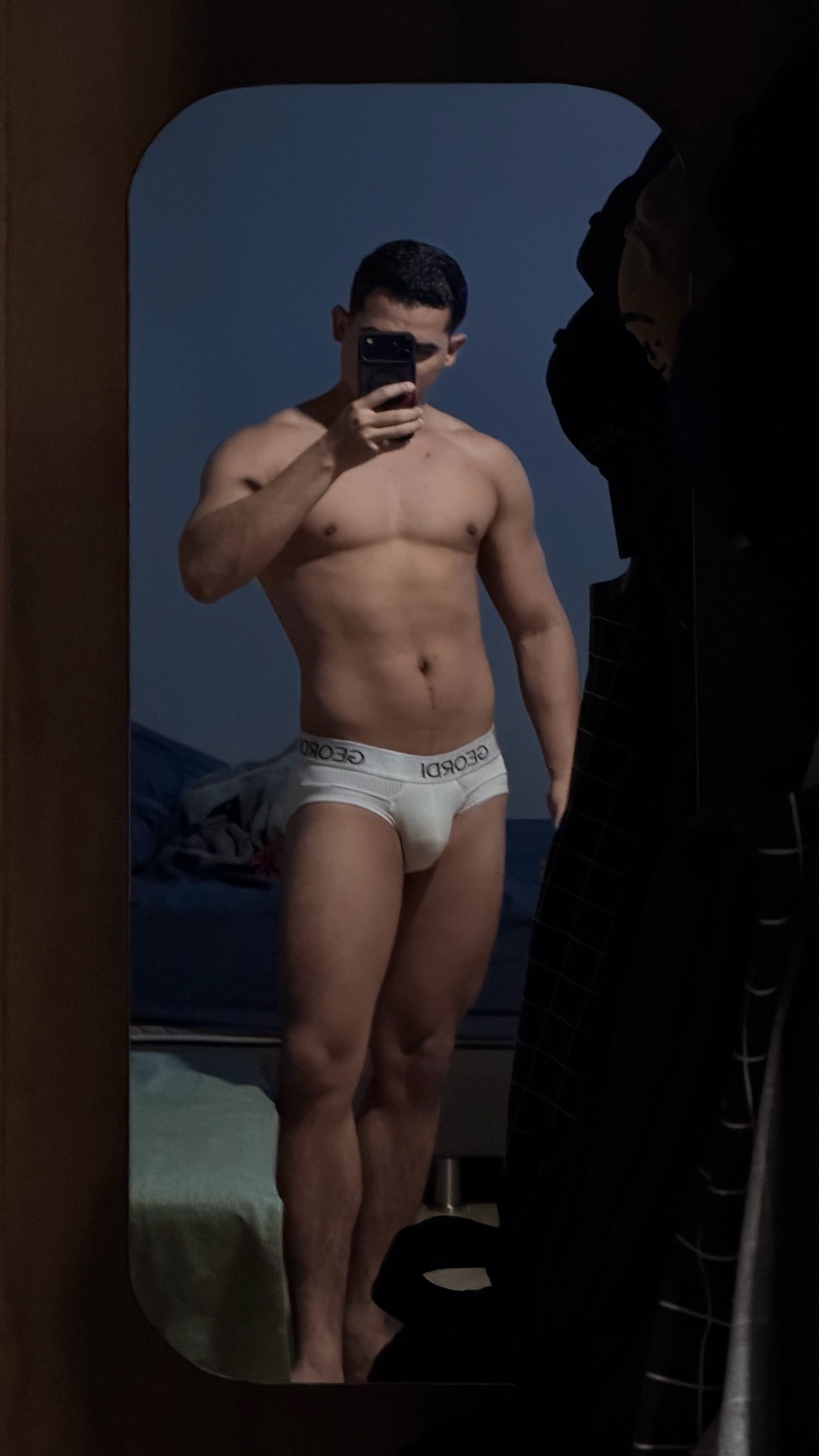 A man in white underwear takes a mirror selfie, showing off his muscular physique.