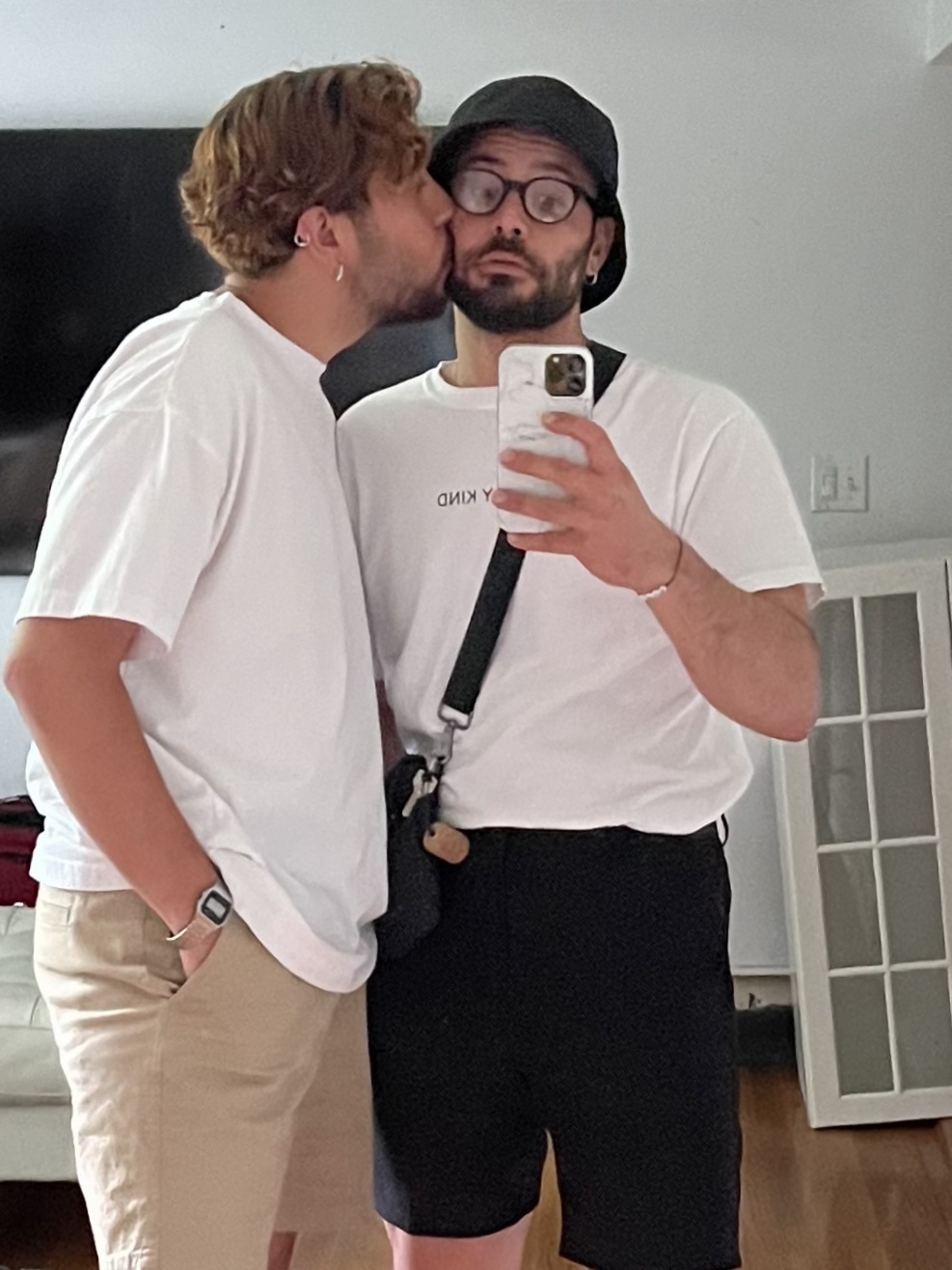 A selfie of a couple kissing. Both men are wearing casual outfits.