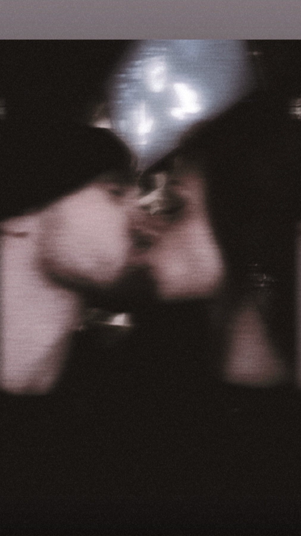 A blurry photo of a couple kissing. The image is dark, with the subjects' faces close together.