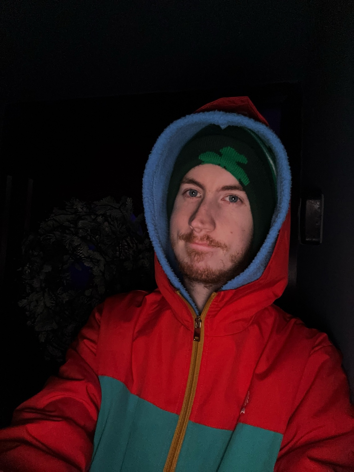 A man in a red and blue hoodie and a green beanie. He is looking at the camera with a slight smile.