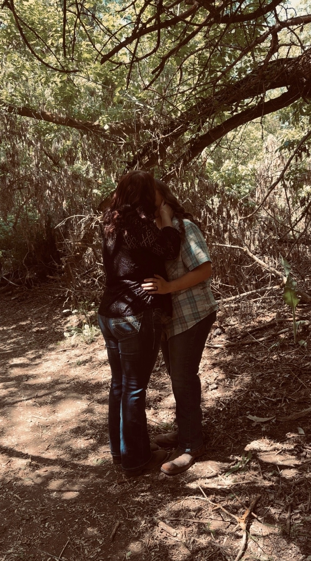 A couple kissing in a wooded area. They are embracing under a tree.