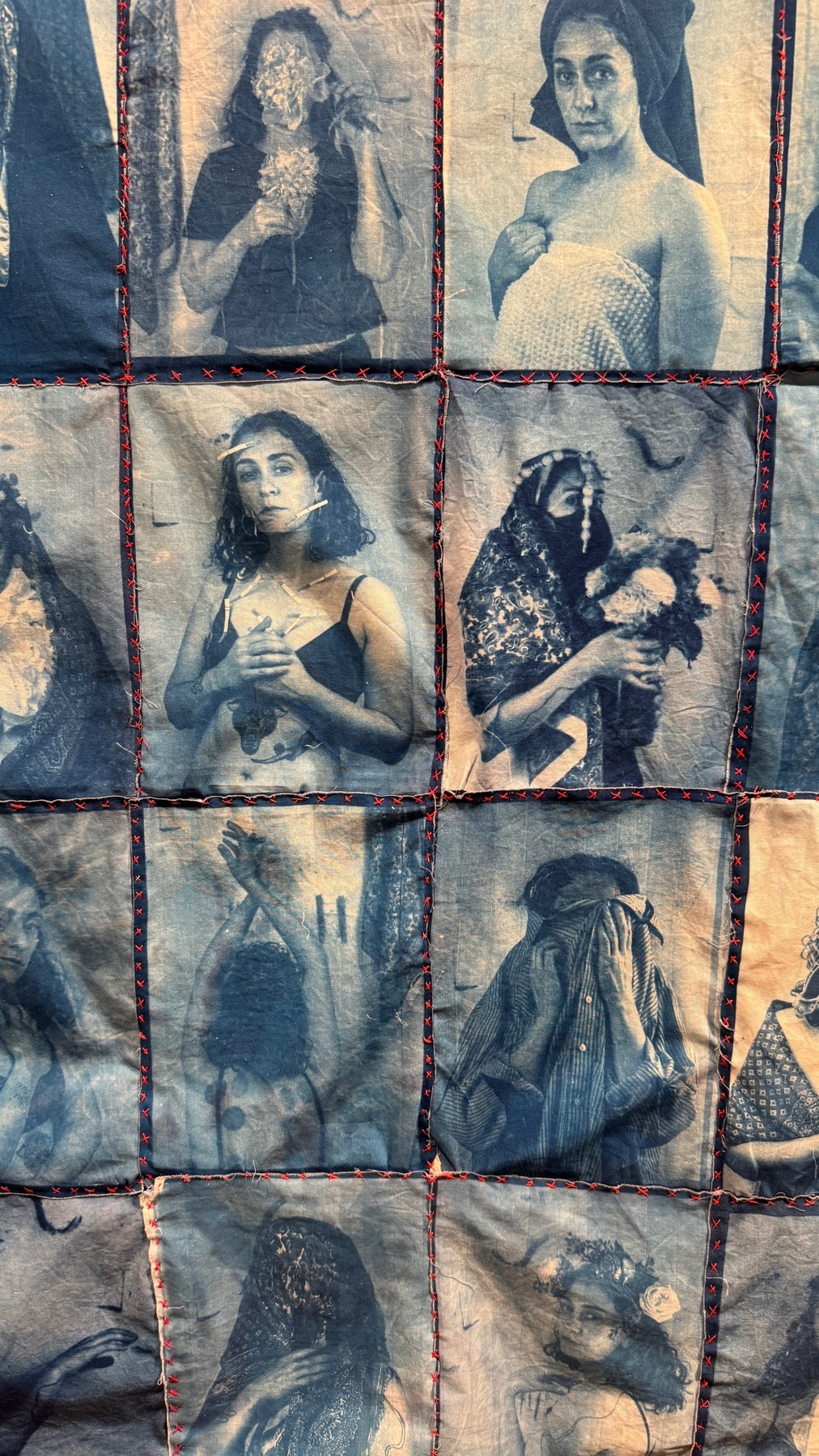 A close-up of a cyanotype collage featuring multiple portraits of women. The images are printed on fabric squares stitched together with red thread, creating a unique textile art piece.