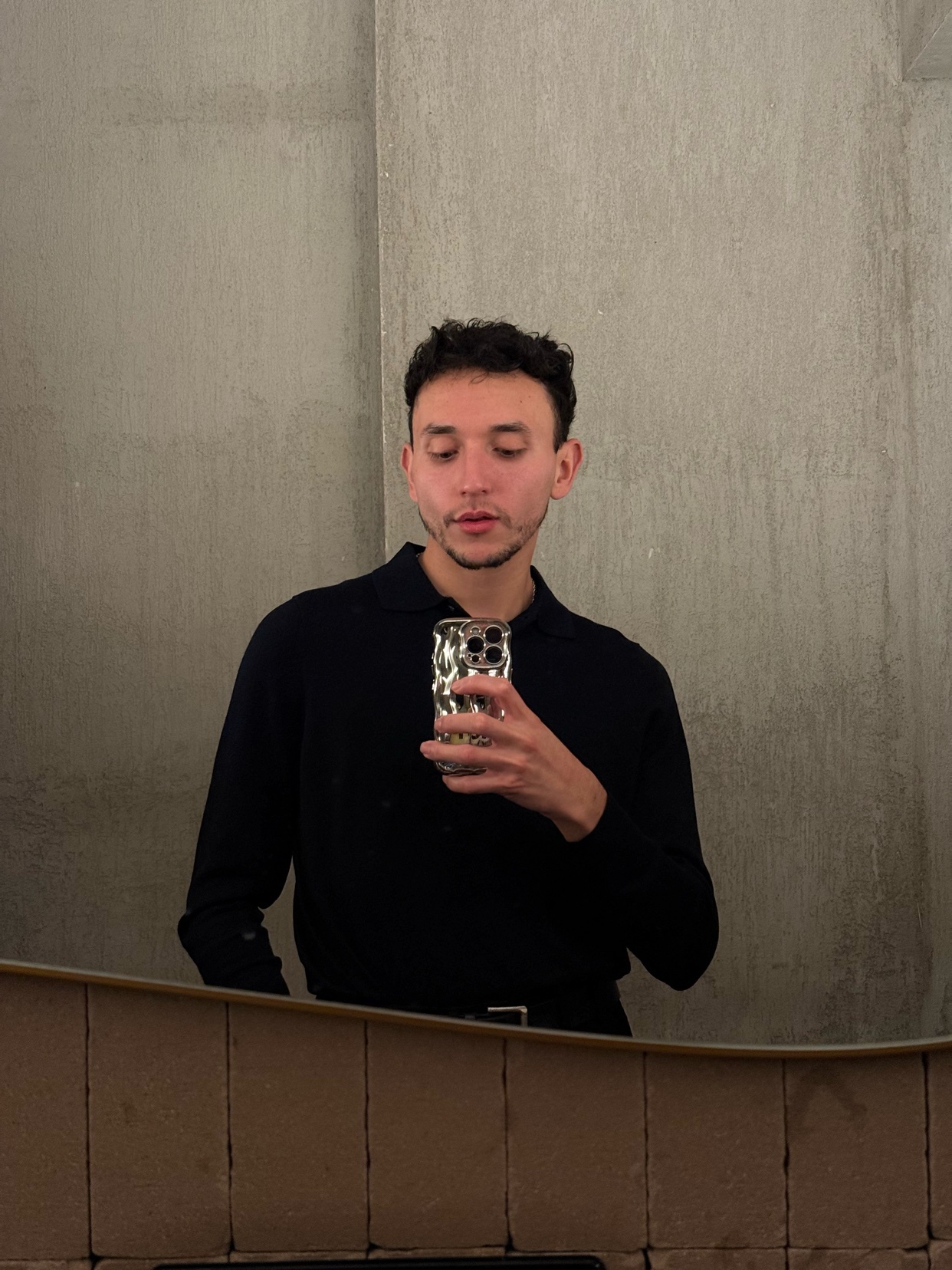 A man takes a mirror selfie. He is wearing a black shirt.