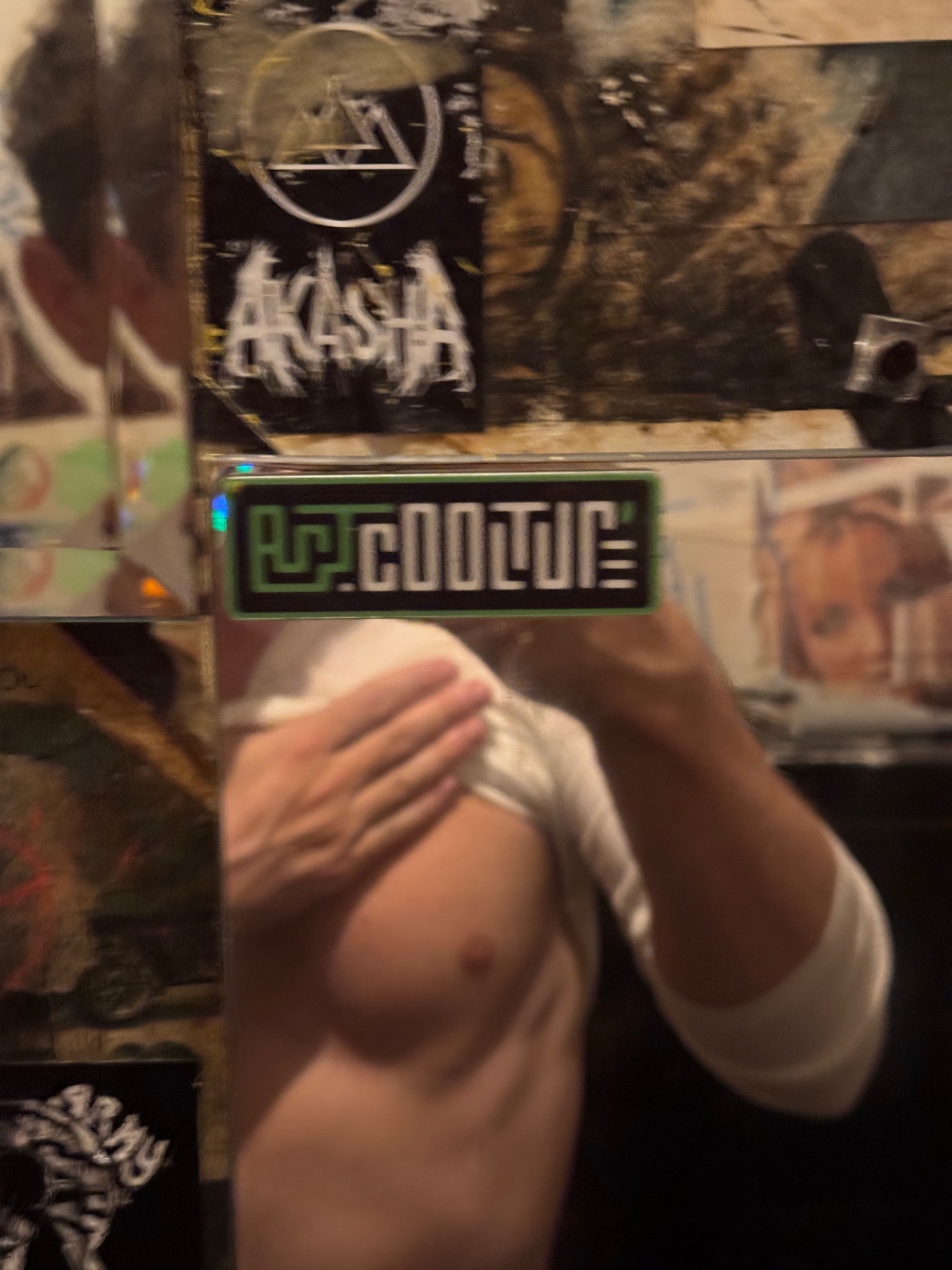 A man takes a mirror selfie, shirtless, with a tattoo visible. The photo is taken in a bathroom.