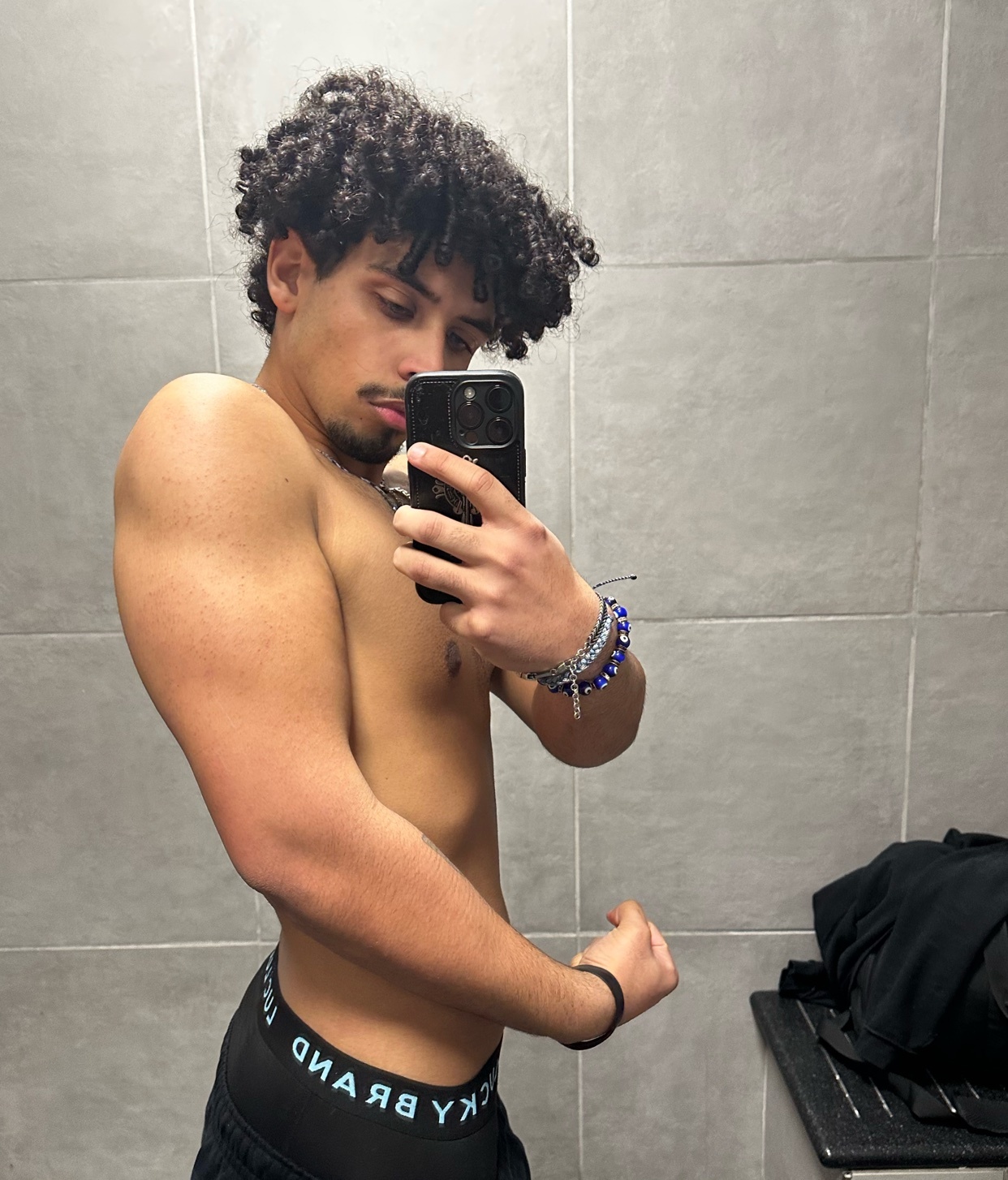 A man takes a selfie in a gym, flexing his bicep. He is shirtless and wearing underwear.