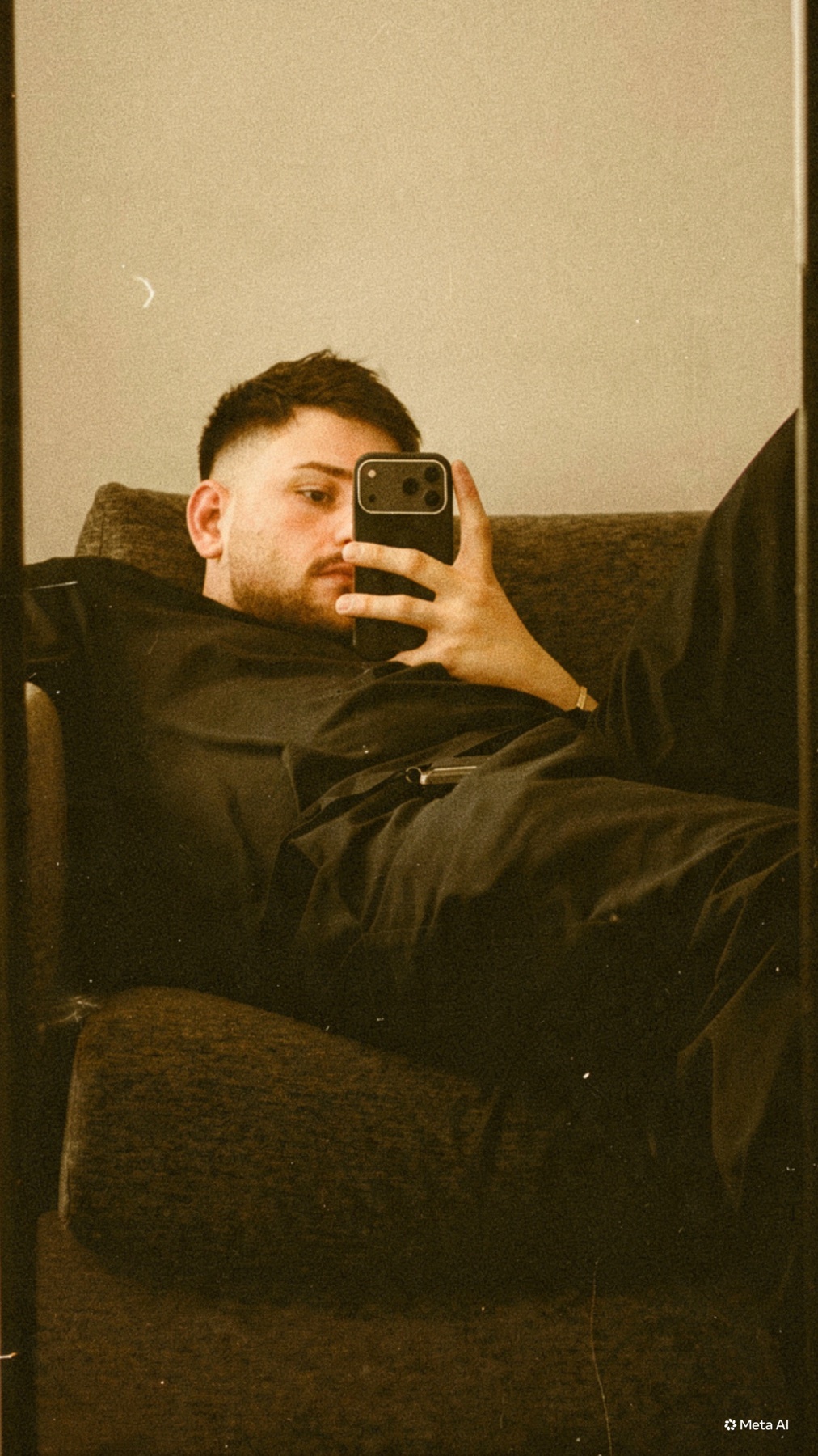 A man takes a mirror selfie while lounging on a couch, holding his phone up to capture the shot.
