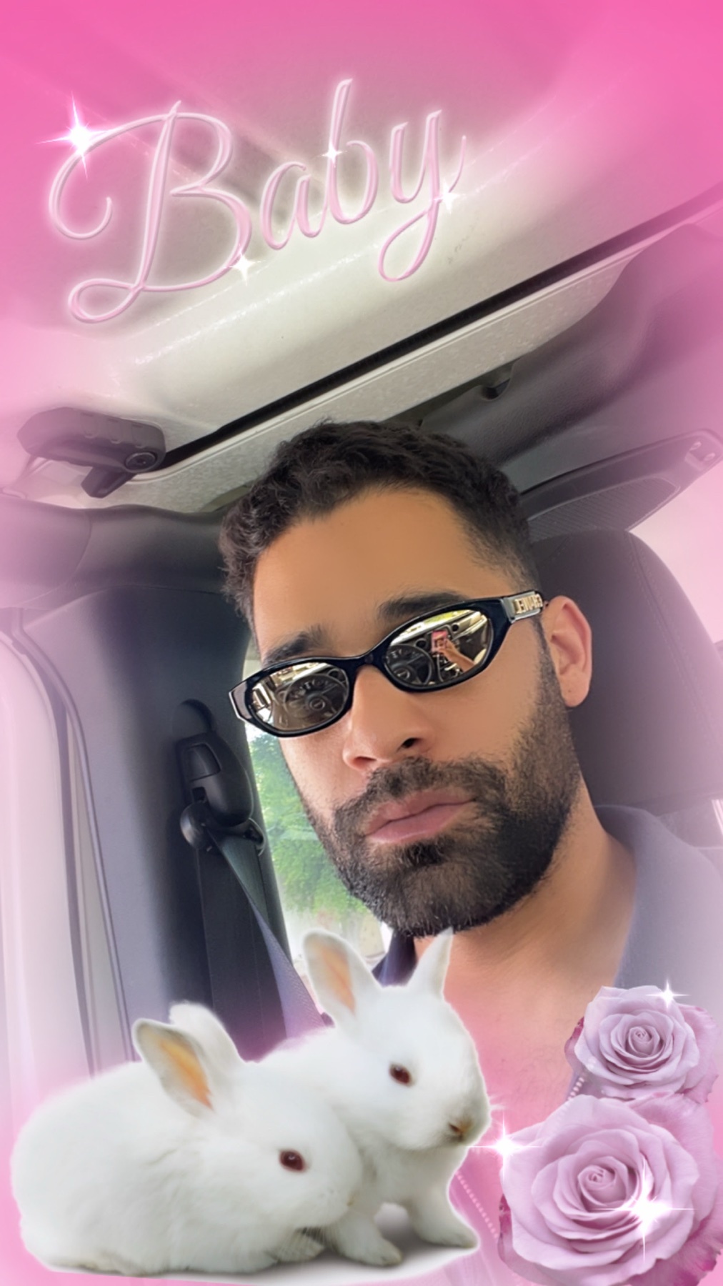 A man wearing sunglasses takes a selfie. The image is overlaid with a pink filter and features two bunnies and roses.