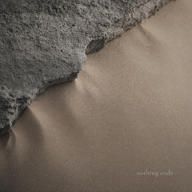 A close-up abstract image shows the rough texture of a dark gray rock meeting a smooth, tan surface that appears to be sand. The text 'nothing ends' is subtly placed in the lower right corner.