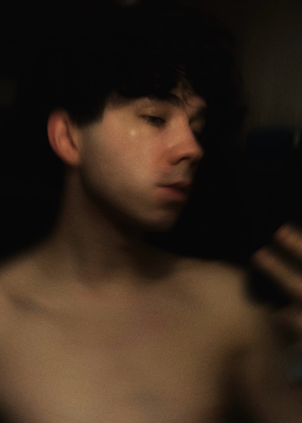 A blurry selfie of a man, shirtless, with dark hair. The photo has a warm, golden tone.